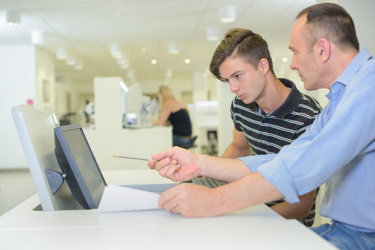 Man pointing to computer, sitting next to teenager in office