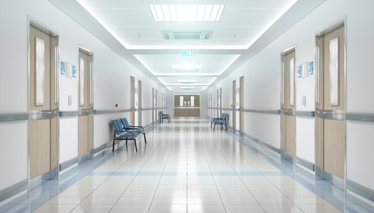 The hospital hallway is empty with blue chairs along the walls.