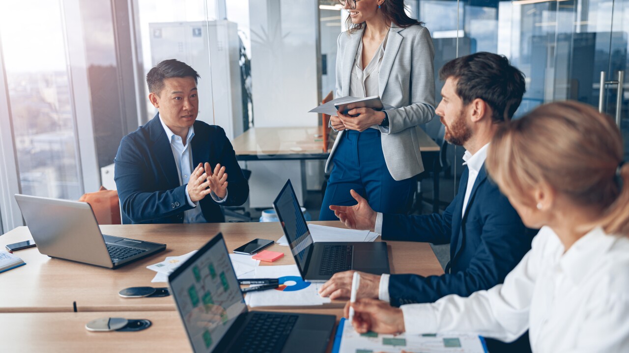 Group of employees sitting at table collaborating with laptops