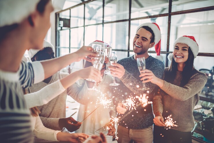 Colleagues with Santa hats toast with champagne glasses.