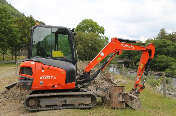 An orange Kubota excavator sits beside a stream.
