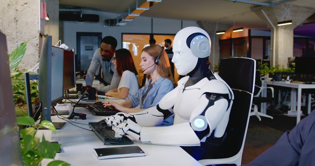 Robot working at computer among people.