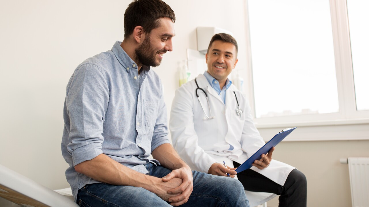 A man in his 40s sits next to a doctor who is holding his patient chart. They are both smiling.