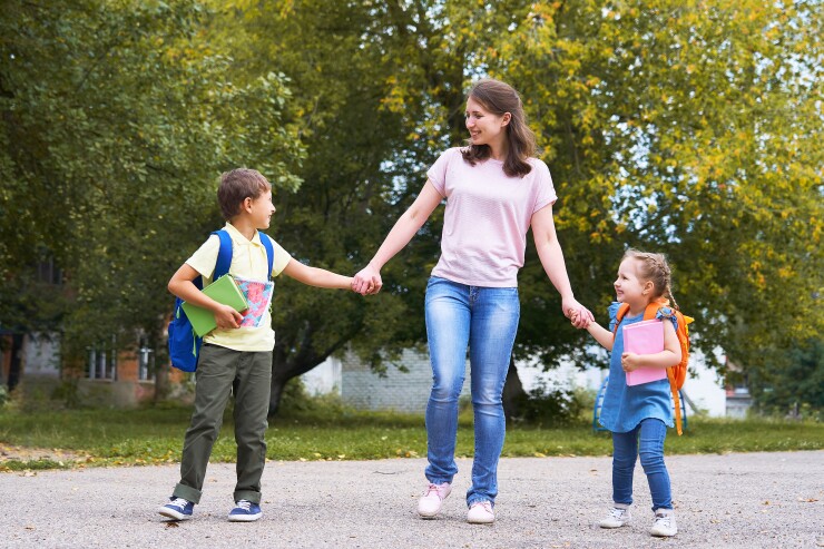 Young woman holding hands with two young children walking to school