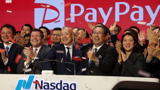 Smiling executives clap and cheer at a Nasdaq opening ceremony with a large PayPay logo and red confetti in the air.