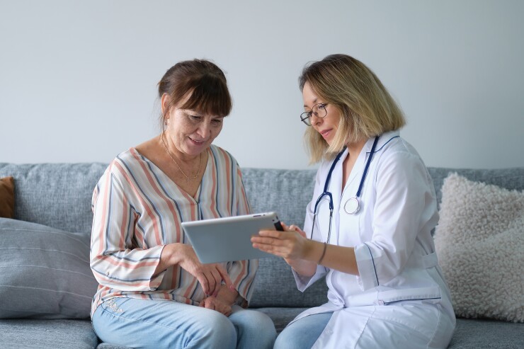 Middle-aged woman sitting on couch with doctor looking at tablet