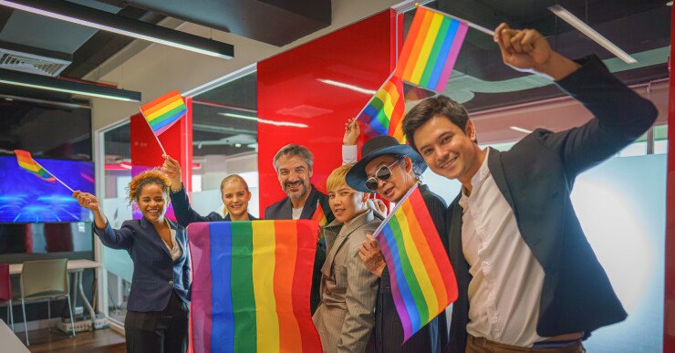Colleagues wave rainbow flags in the office together.
