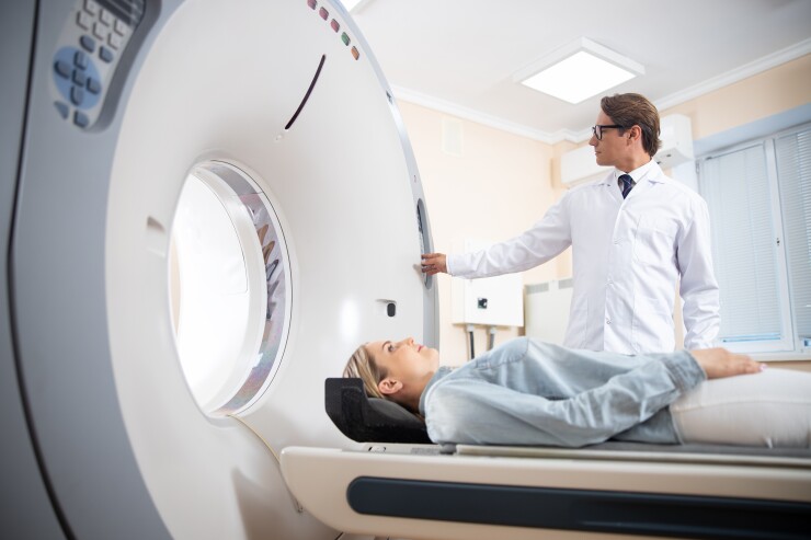 A woman is entering an MRI machine, while a doctor presses a button beside her.