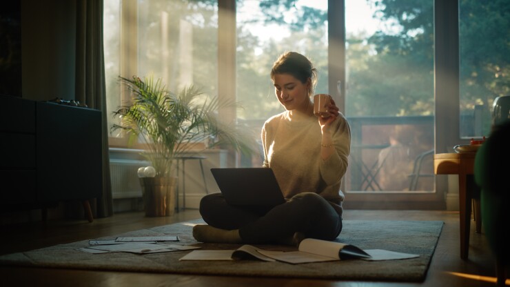 A young employee sits on her living room floor with her laptop.