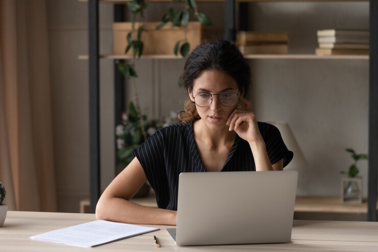 Close up thoughtful businesswoman in glasses looking at laptop screen