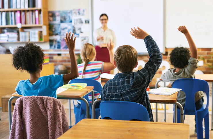 Education, question with group of children in classroom and raise their hands to answer. Learning or support, diversity and teacher teaching with young students in class of school building together.