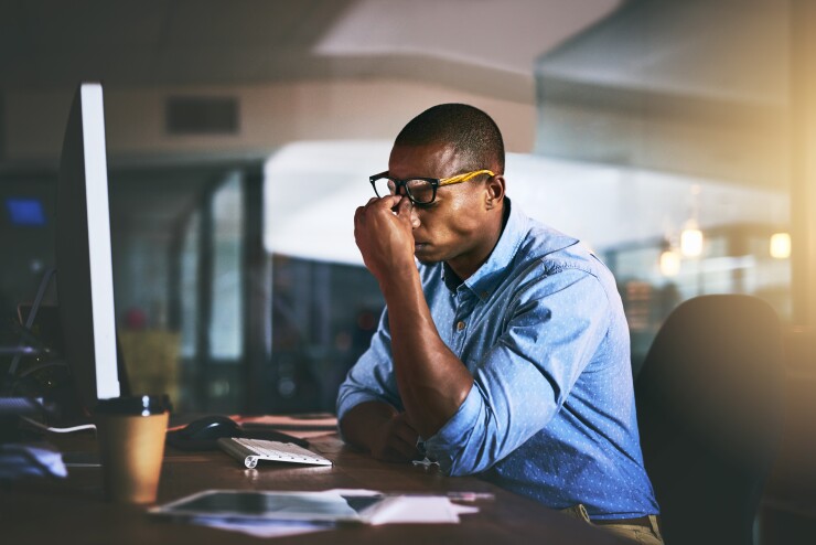 Man sitting at desk, pinching nose, stressed