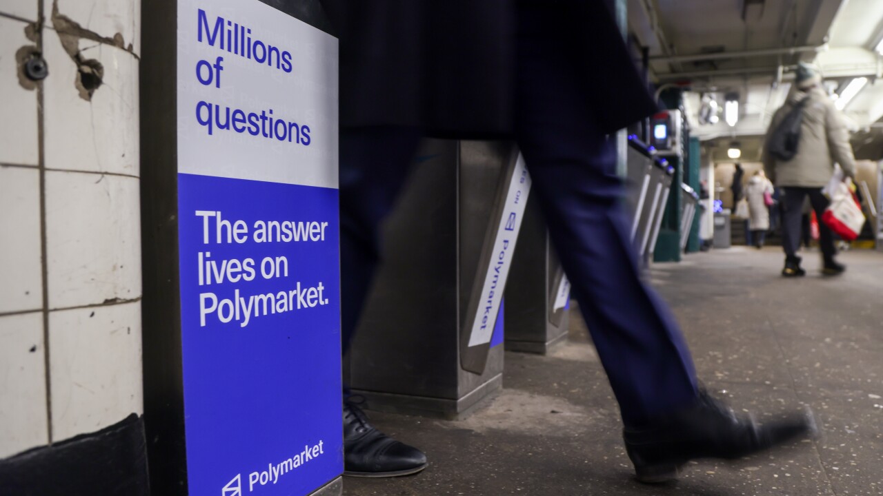 A person walks past a subway turnstile featuring a blue and white Polymarket ad that reads, "Millions of questions. The answer lives on Polymarket."