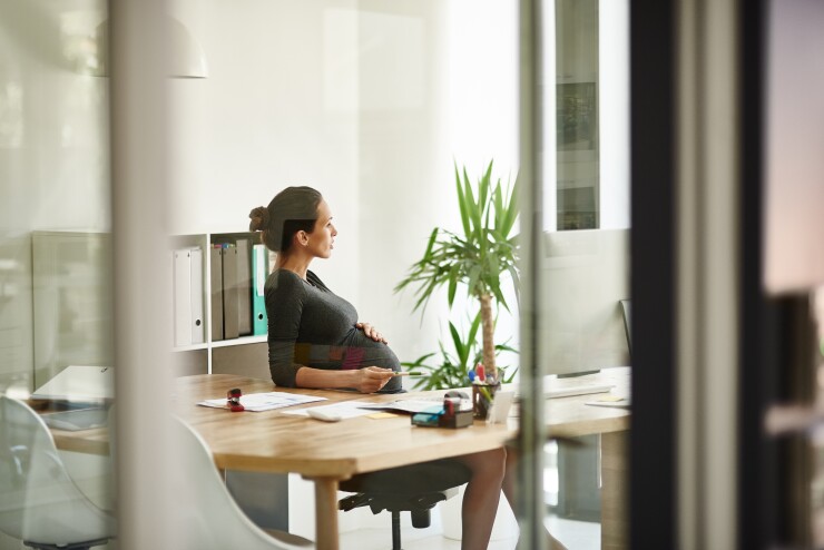 A pregnant woman sitting at her office desk, lost in thought.