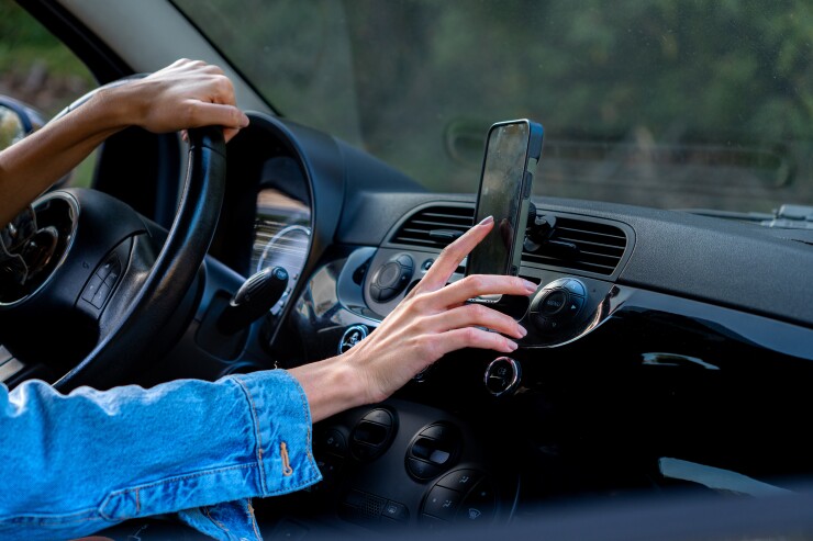 A person driving a car and checking their phone that is mounted.