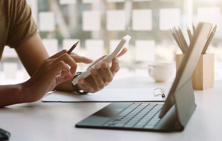 Person typing on calculator and looking at laptop