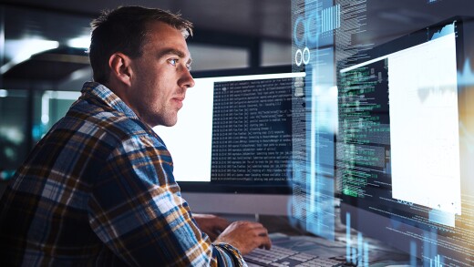 Man sitting in front of two computer screens with data on them.