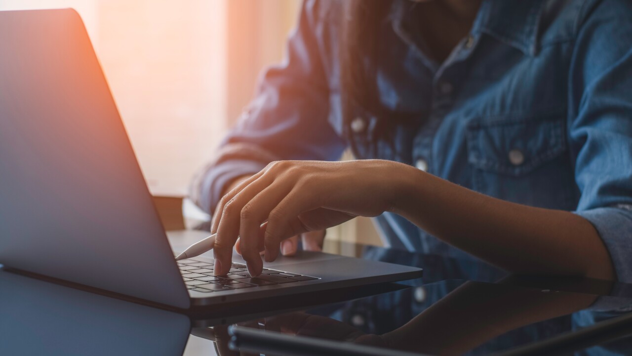 A person using a laptop with a stylus and a tablet near them.
