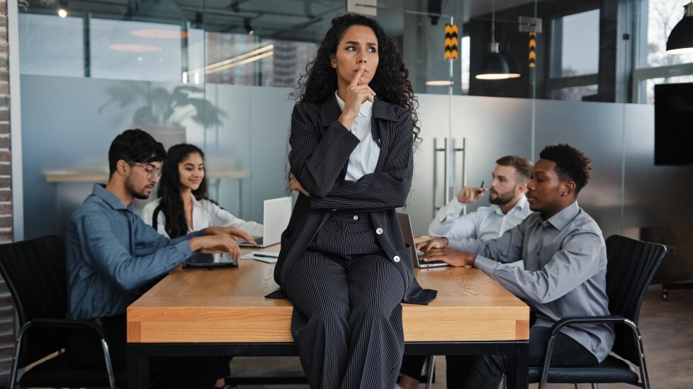 Pensive thinking female company CEO thoughtful businesswoman sitting on table office desk in boardroom think multicultural employees multiethnic workers colleagues work meeting brainstorm background
