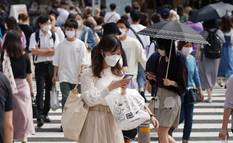 A woman looks at a phone while crossing a road in the Harajuku district of Tokyo, Japan, on Saturday, Oct. 9, 2021. In Japan, vaccinations rates are up, infection case are way down, and the emergency lifted at the start of October. That’s boosting optimism that spending may rebound in coming months as new Prime Minister Fumio Kishida launches his administration. Photographer: Toru Hanai/Bloomberg