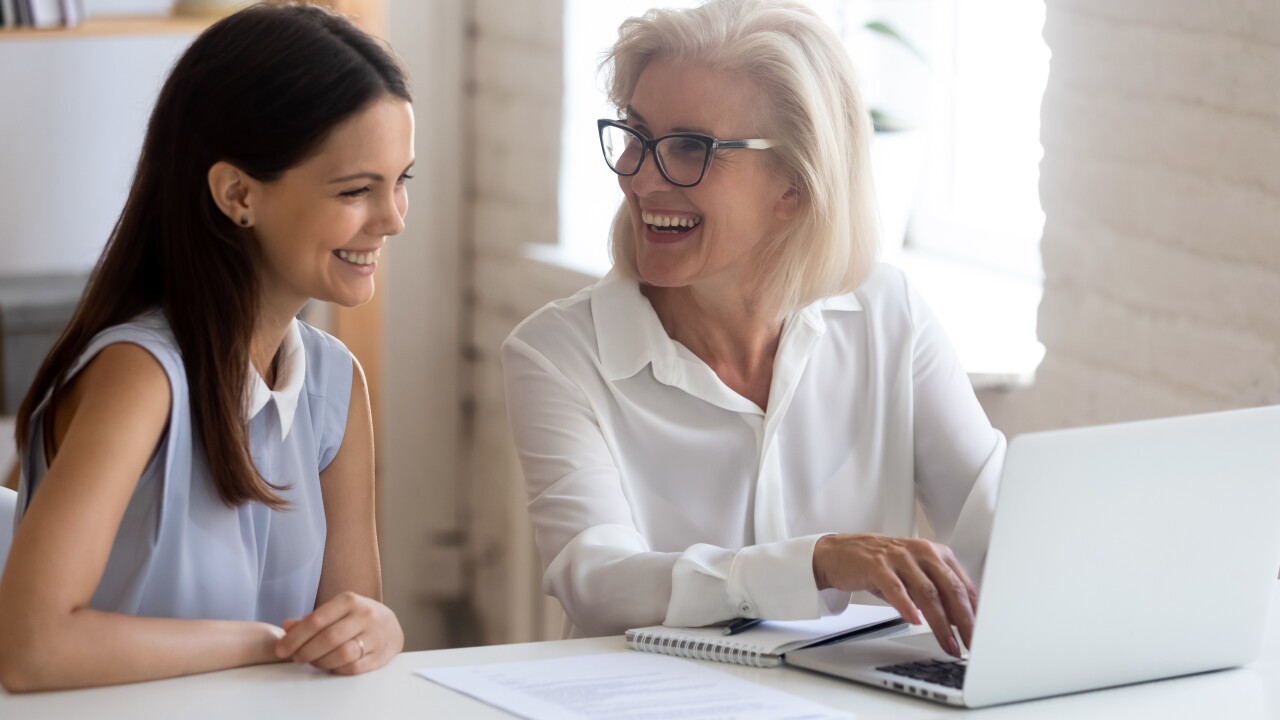 Older employee with younger employee, working on laptop and laughing