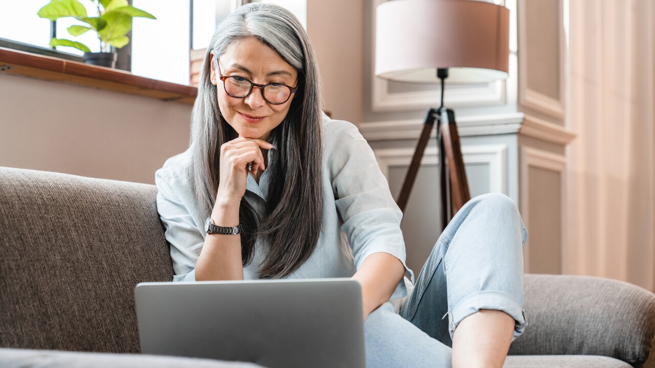 Woman sitting on couch, long gray hair and glasses, looking at computer