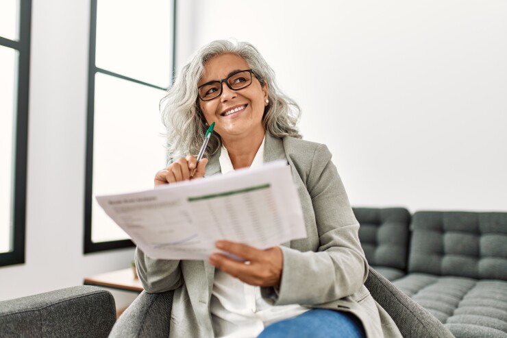Woman holding papers, pressing pen to her cheek, thinking, smiling