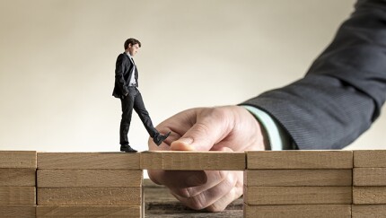 Helping business associates succeed (image showing hand of large executive holding a walkway for a much smaller executive).