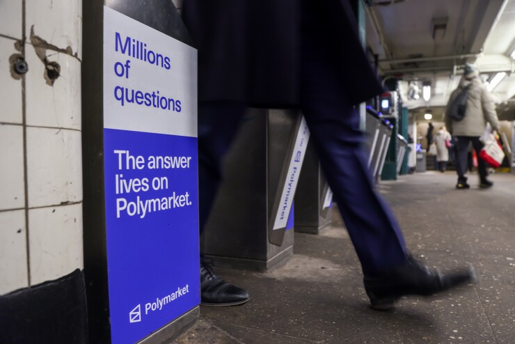 A person walks past a subway turnstile featuring a blue and white Polymarket ad that reads, "Millions of questions. The answer lives on Polymarket."