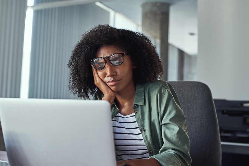 A young Black woman looks at her laptop in frustration.