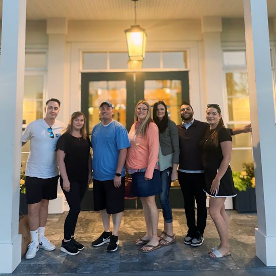 Group of PayQuicker employees in casual clothes stand together for a photo in between two white pillars.