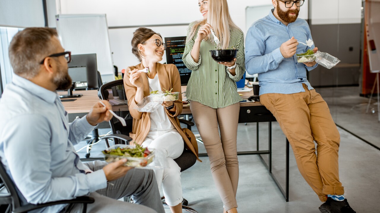 Employees eating, standing and sitting at desk
