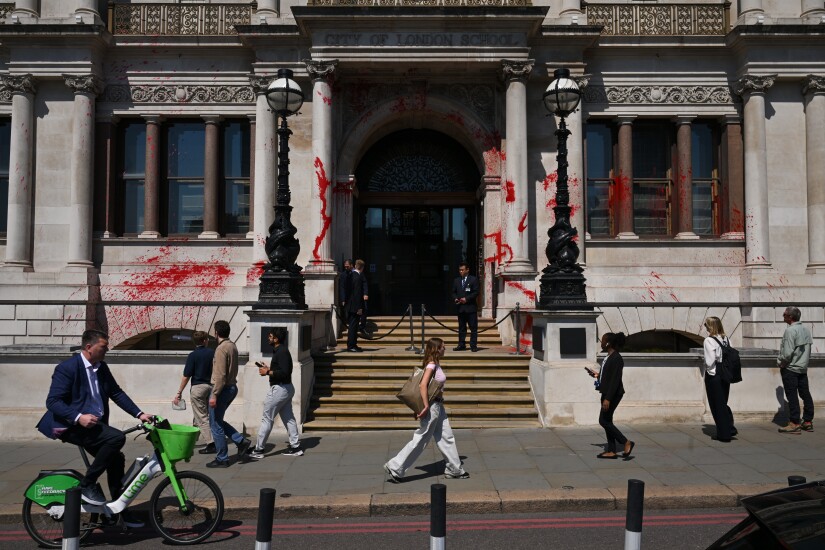 The ornate Victorian front of the JPMorganChase building in the City of London has been sprayed with red paint. Three men in suits stand at the entrance, preventing public access.