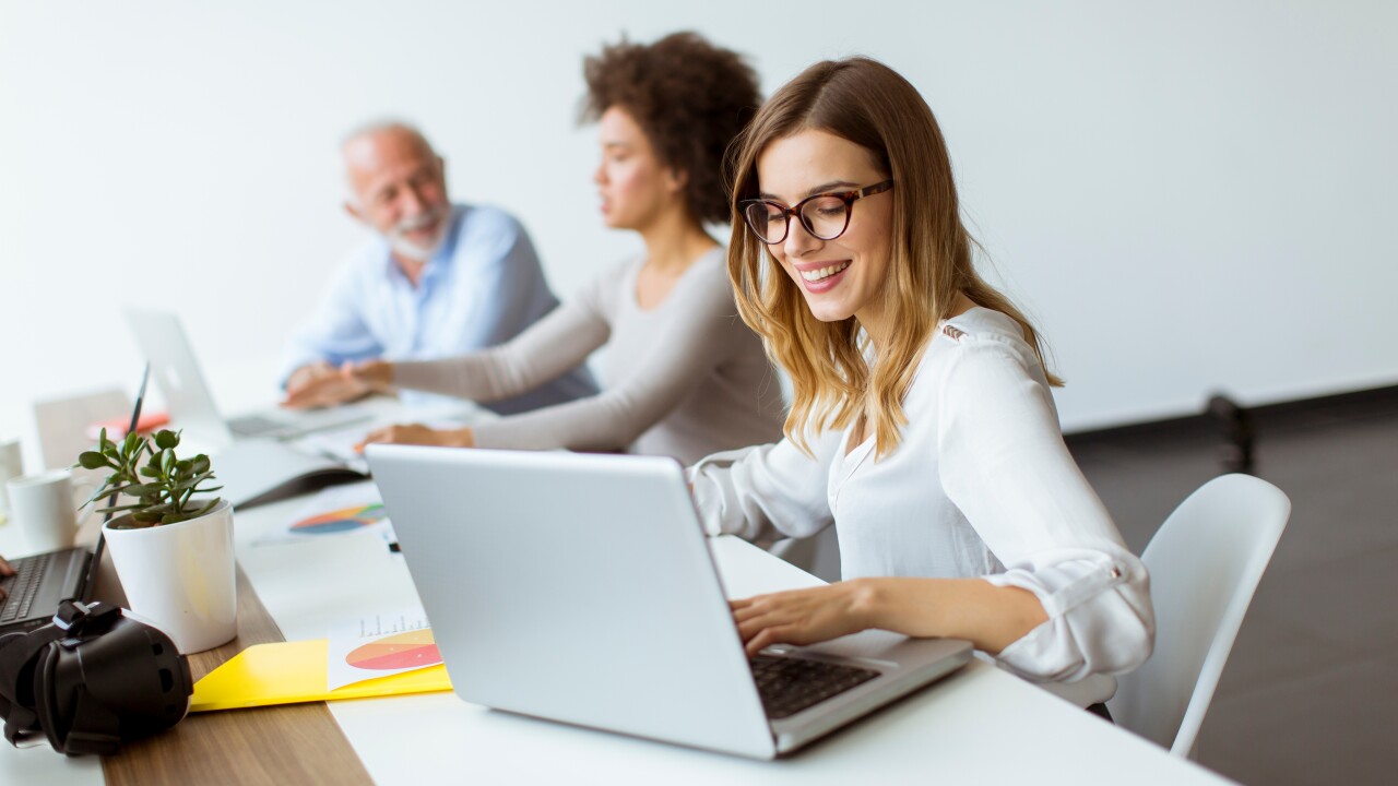 People working at long desk, female employee working on laptop, smiling