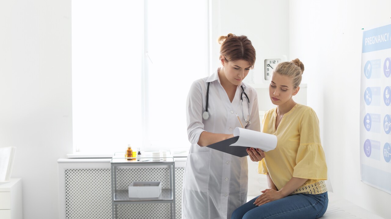 Young woman sitting on exam table at doctor's office with female doctor, looking at paperwork