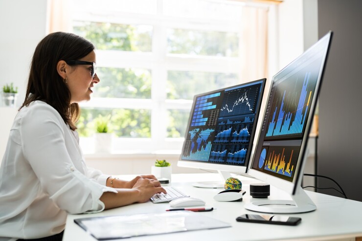 Woman working in front of two computer screens looking at data.