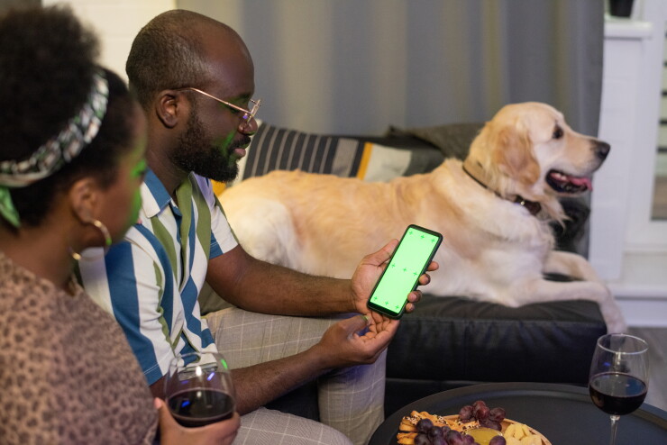 People watching a screen of a mobile phone while sitting on sofa with a dog.