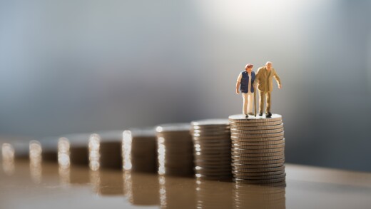 Small wax figures of an elderly couple sit on top of the largest pile of coins in a series of expanding numbers of coins, signifying retirement savings