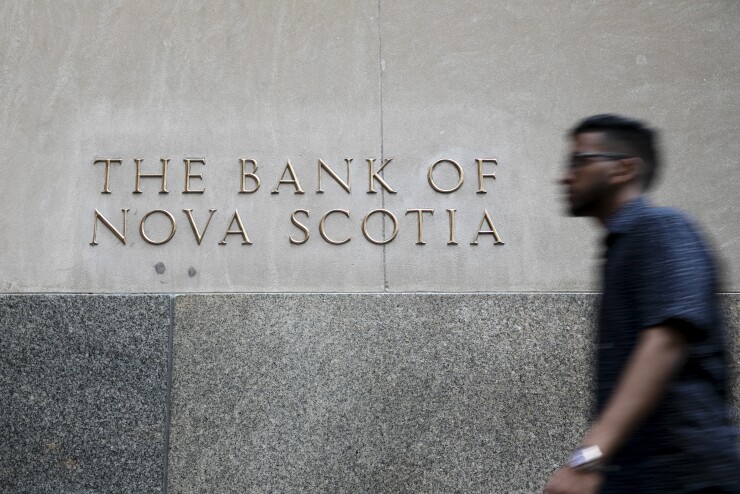 A pedestrian passes in front of a building displaying The Bank of Nova Scotia signage in the financial district of Toronto.