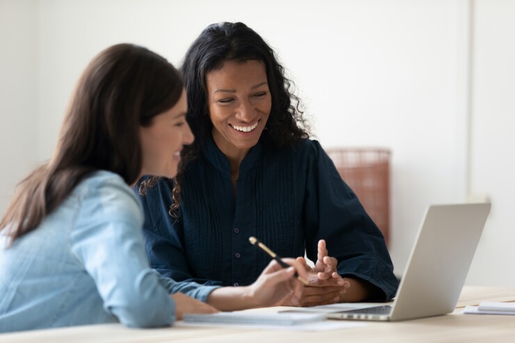 Two women chat in front of a laptop.