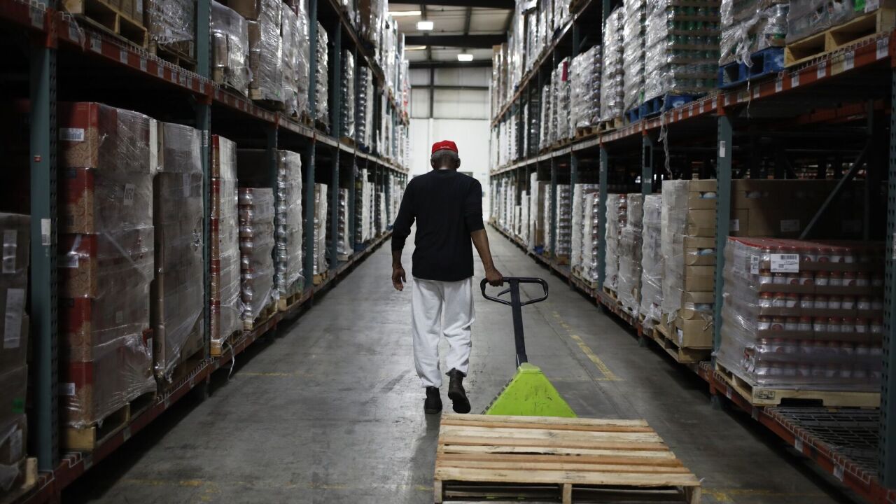 Worker in warehouse pulling pallet on wheels down aisle