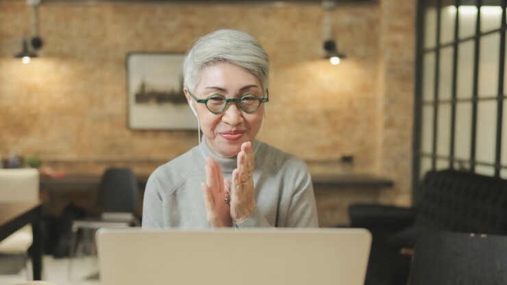 Older woman sitting in front of a computer and clapping her hands.