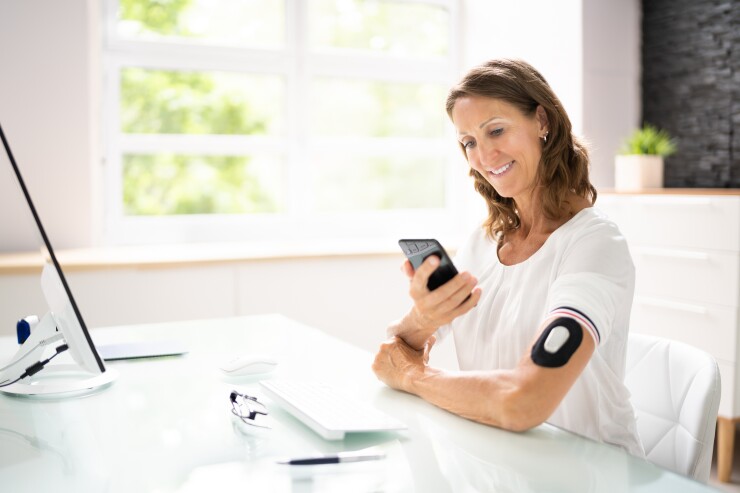 Woman sitting at desk wearing glucose monitor looking at phone