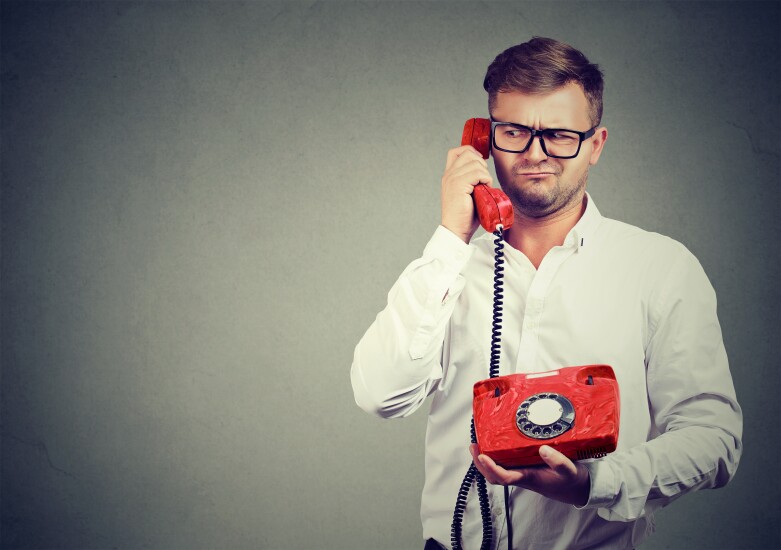 Casual man in eyeglasses talking on old-fashioned phone looking away in misunderstanding.