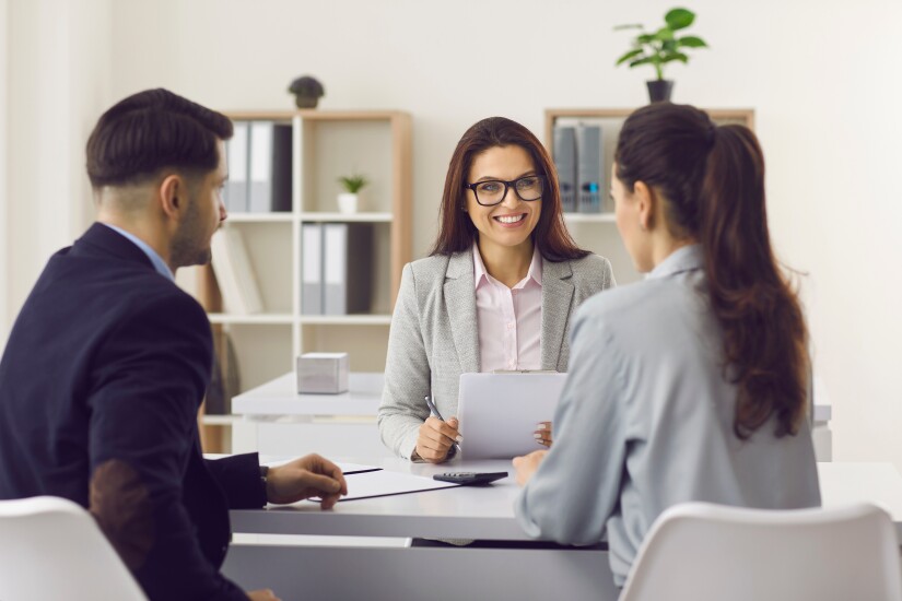 A person talking to two other people across a desk.