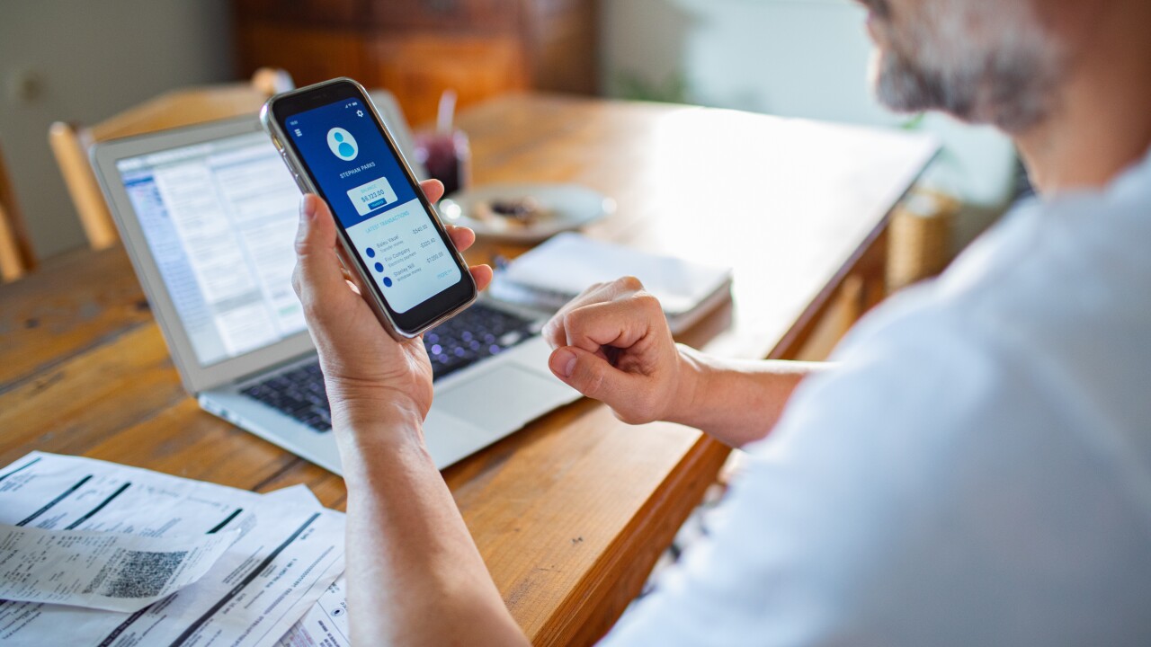 Man looking at cell phone, personal account, laptop on table