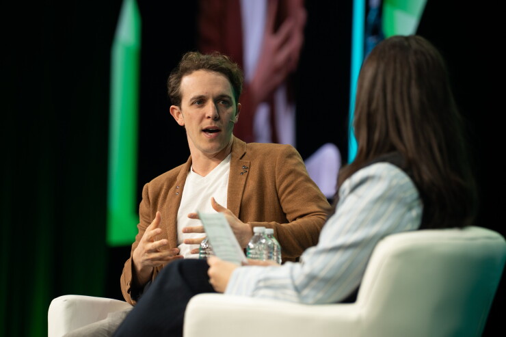 Bolt CEO Ryan Breslow at Fintech Meetup 2026Man in brown jacket and white shirt sits in a chair on a stage, speaking to a female moderator in the foreground.
