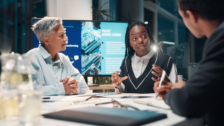 People in a meeting together around a table with a screen in the back that reads project machine learning