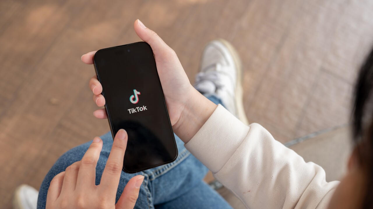 A close-up shot of a woman using the TikTok application on her iPhone while sitting outdoor.