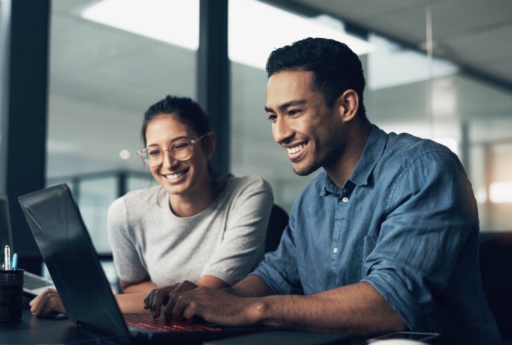 Two colleagues smile as they look at a laptop.